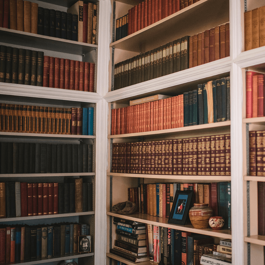 Corner of a library with white shelves full of vintage books, pottery and photos.