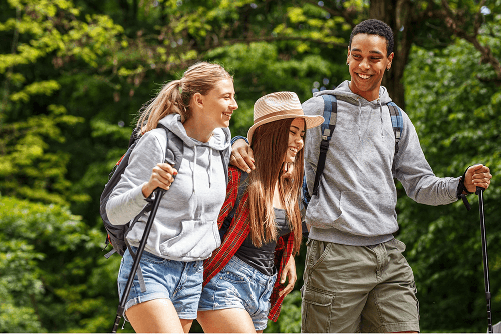 two women and one man with backpacks and hiking poles in woods